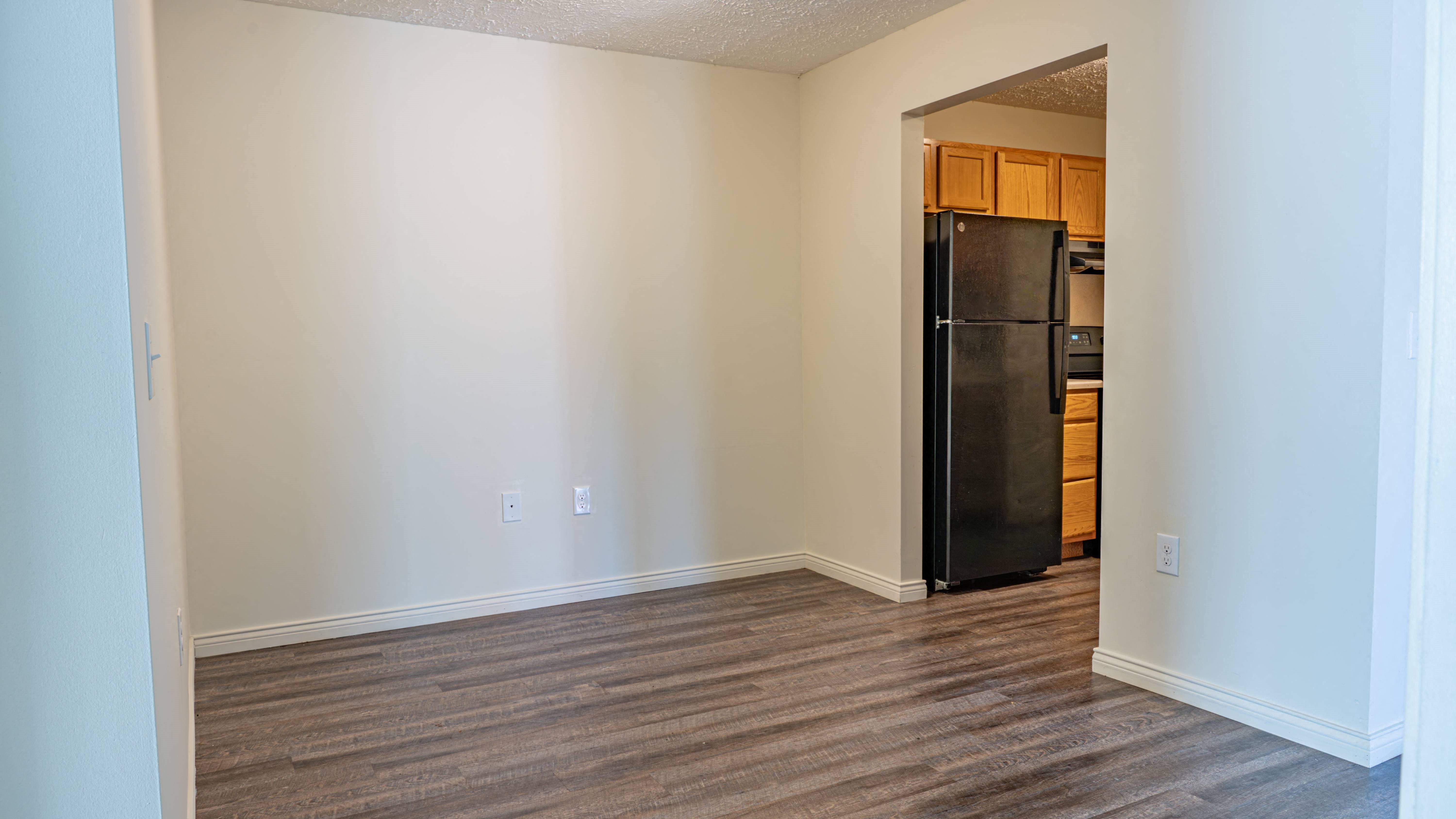 an empty living room with wood flooring and a black refrigerator
